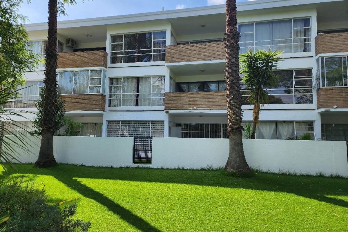 Rear view of a multi-story apartment building featuring brick facade, private balconies, large windows, and a well-maintained communal garden area.