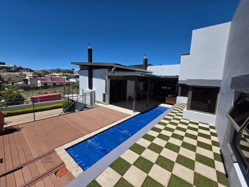 Modern outdoor entertainment area featuring a lap pool, timber decking, and a unique checkered patio design adjacent to the main residence.