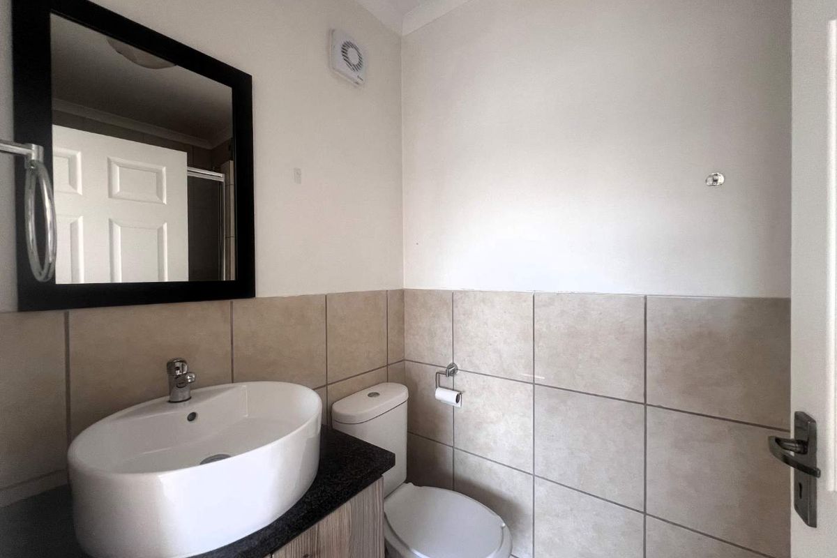 A functional bathroom featuring a vanity with a vessel sink, a toilet, and neutral wall tiling.