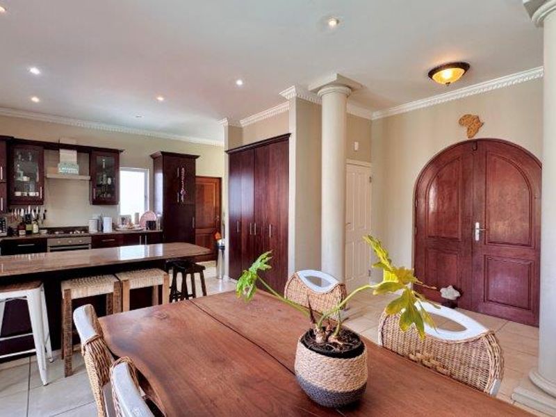 Spacious open-plan kitchen and dining area featuring dark wood cabinetry, granite countertops, decorative columns, and elegant arched double doors.