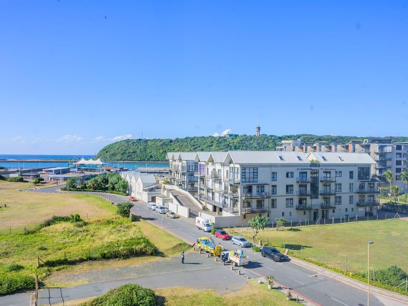 Elevated view overlooking a coastal residential apartment complex, surrounding green spaces, and the nearby harbor area.