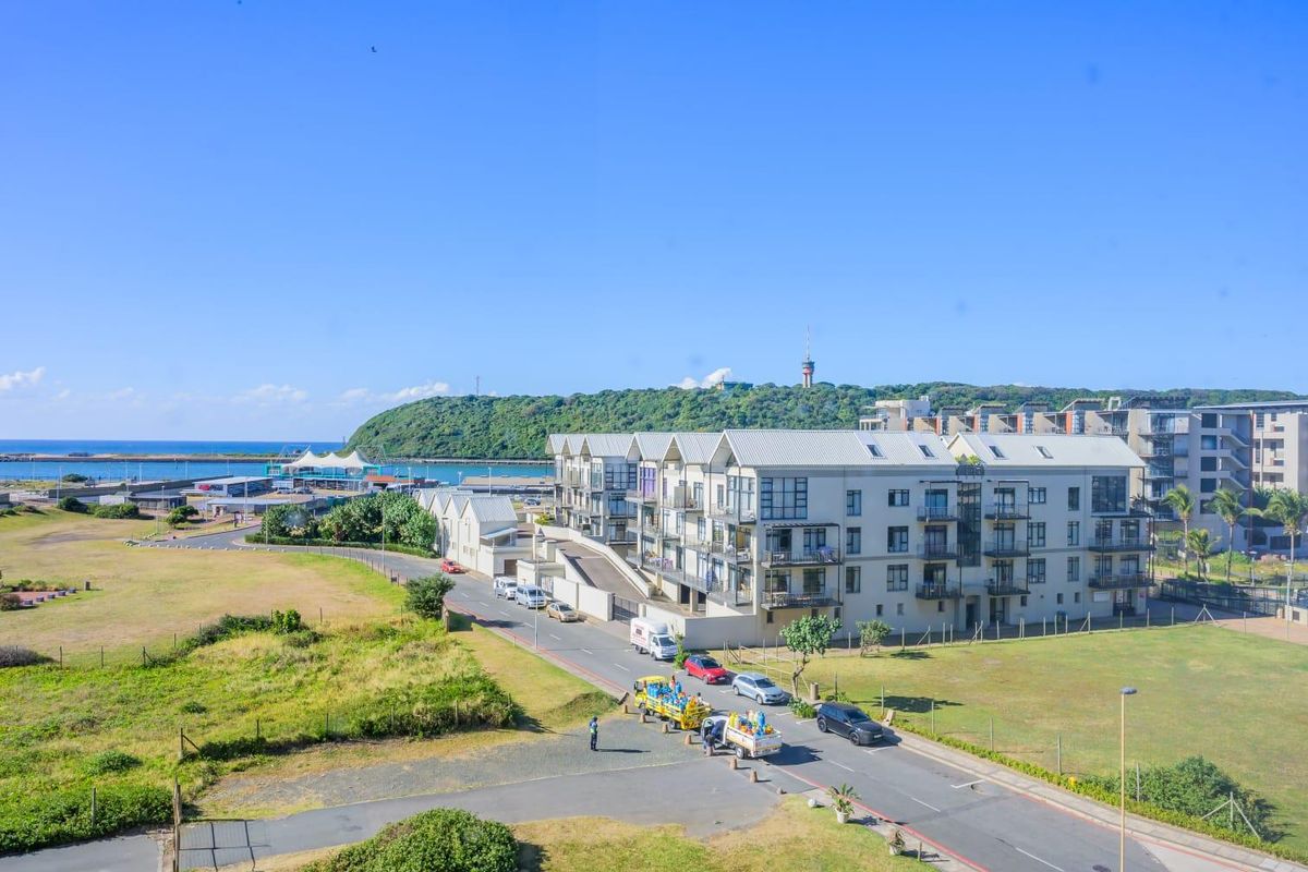 Elevated view overlooking a coastal residential apartment complex, surrounding green spaces, and the nearby harbor area.