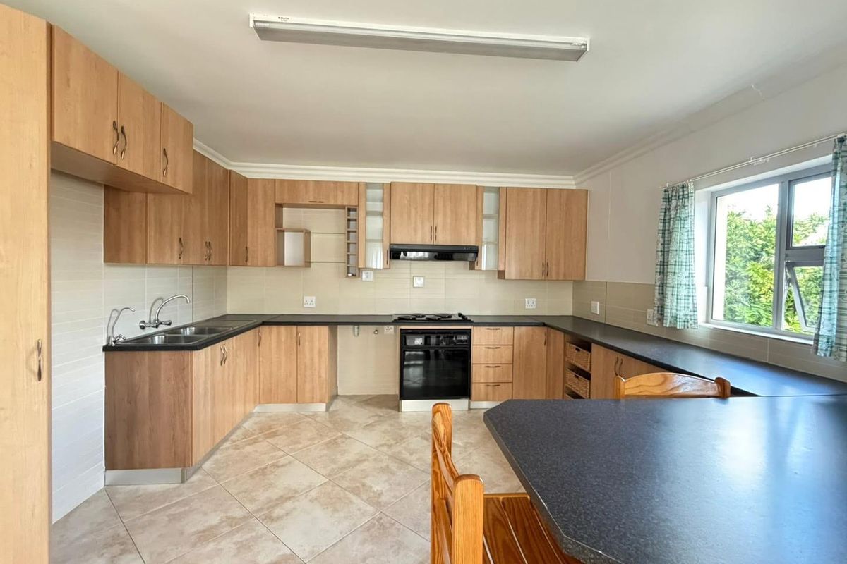 A functional kitchen featuring light wood cabinetry, dark countertops, tiled flooring, a built-in oven, and an extractor fan.