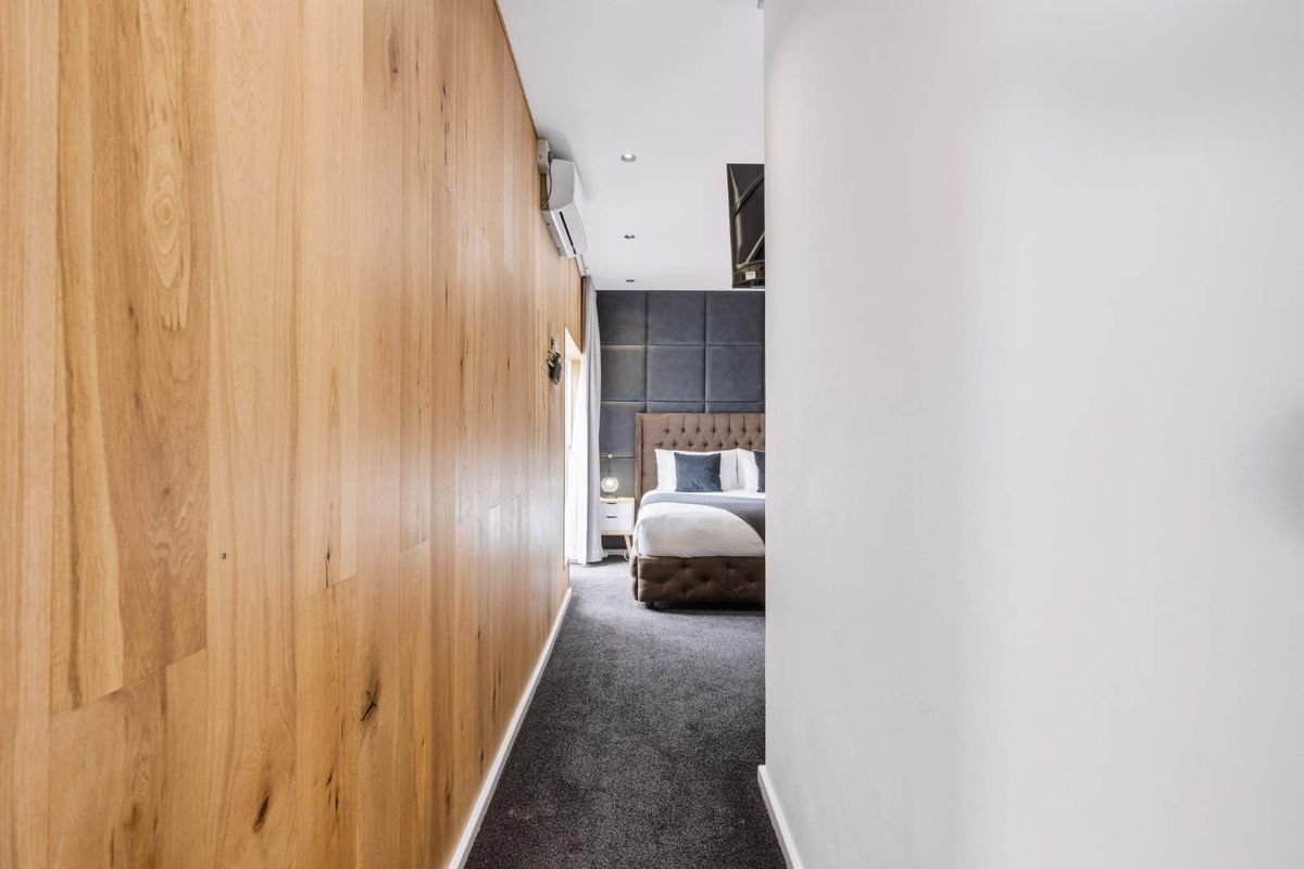 A modern bedroom featuring warm timber wall paneling, a dark upholstered feature wall, and recessed lighting, creating a sophisticated and cozy atmosphere.