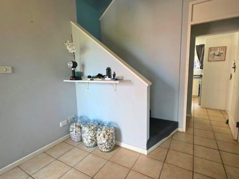 A tiled hallway area featuring a staircase with carpeted steps and access to an adjacent room.