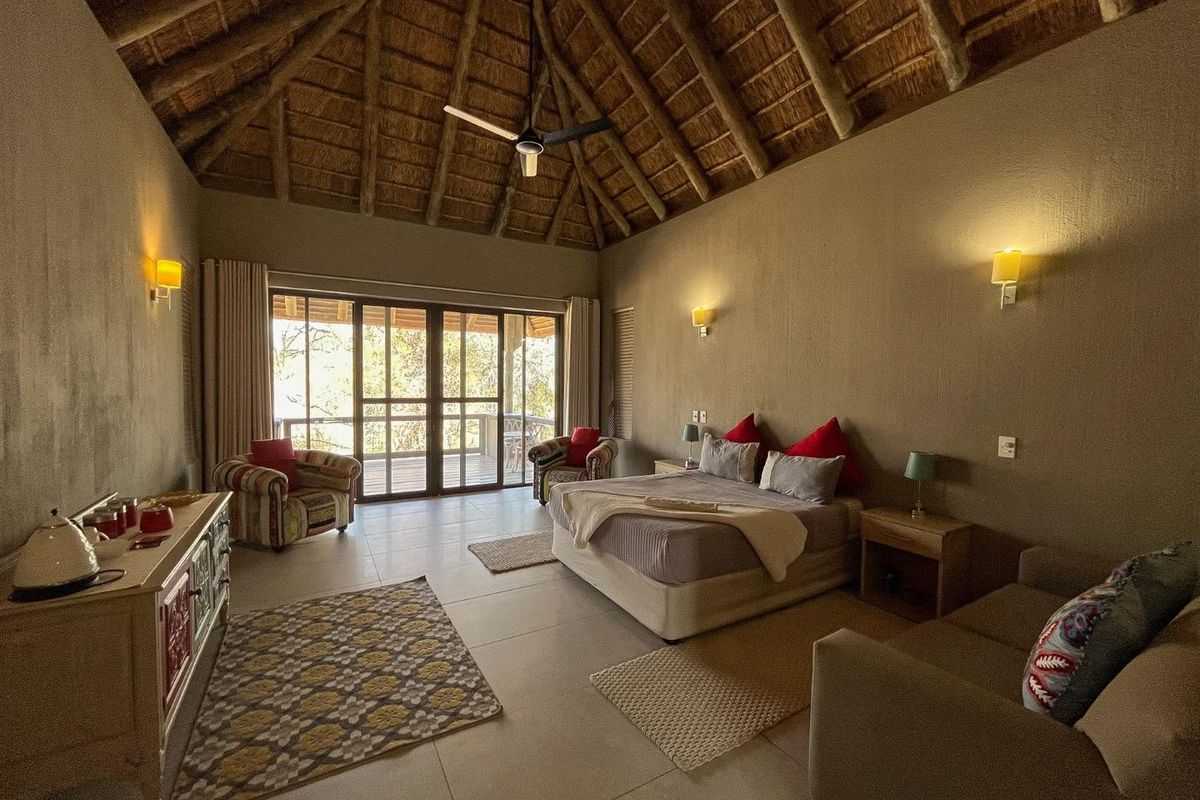 Spacious bedroom featuring a high vaulted thatched ceiling, tiled flooring, and large sliding glass doors opening onto a private balcony.