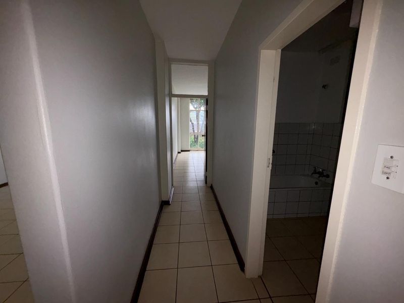 A narrow hallway with tiled flooring leading towards an exterior doorway, with access to an adjacent bathroom.