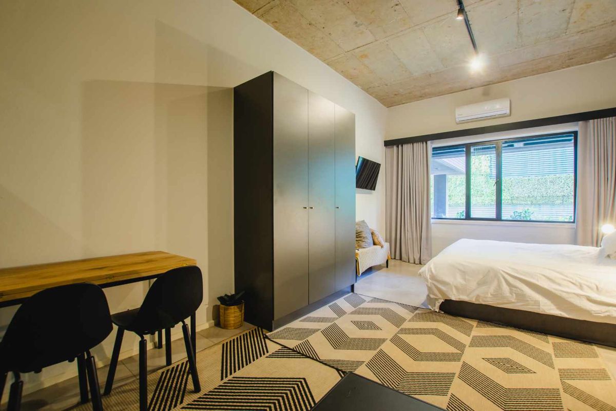 Modern bedroom featuring an exposed concrete ceiling, built-in wardrobe, and wall-mounted air conditioning unit with large window providing natural light.