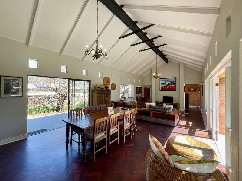 Spacious open-plan living and dining area featuring a dramatic vaulted ceiling with exposed steel beams, herringbone parquet flooring, and large sliding doors to the garden.