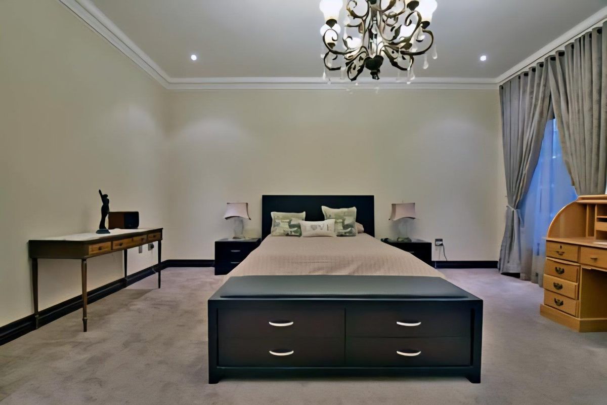 Spacious bedroom featuring neutral wall finishes, plush carpeting, decorative ceiling coving, and a central chandelier, creating a comfortable and well-maintained sleeping environment.