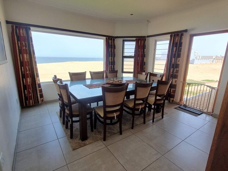 Spacious dining room featuring large windows with direct ocean views, tiled flooring, and seamless access to the outdoor area.