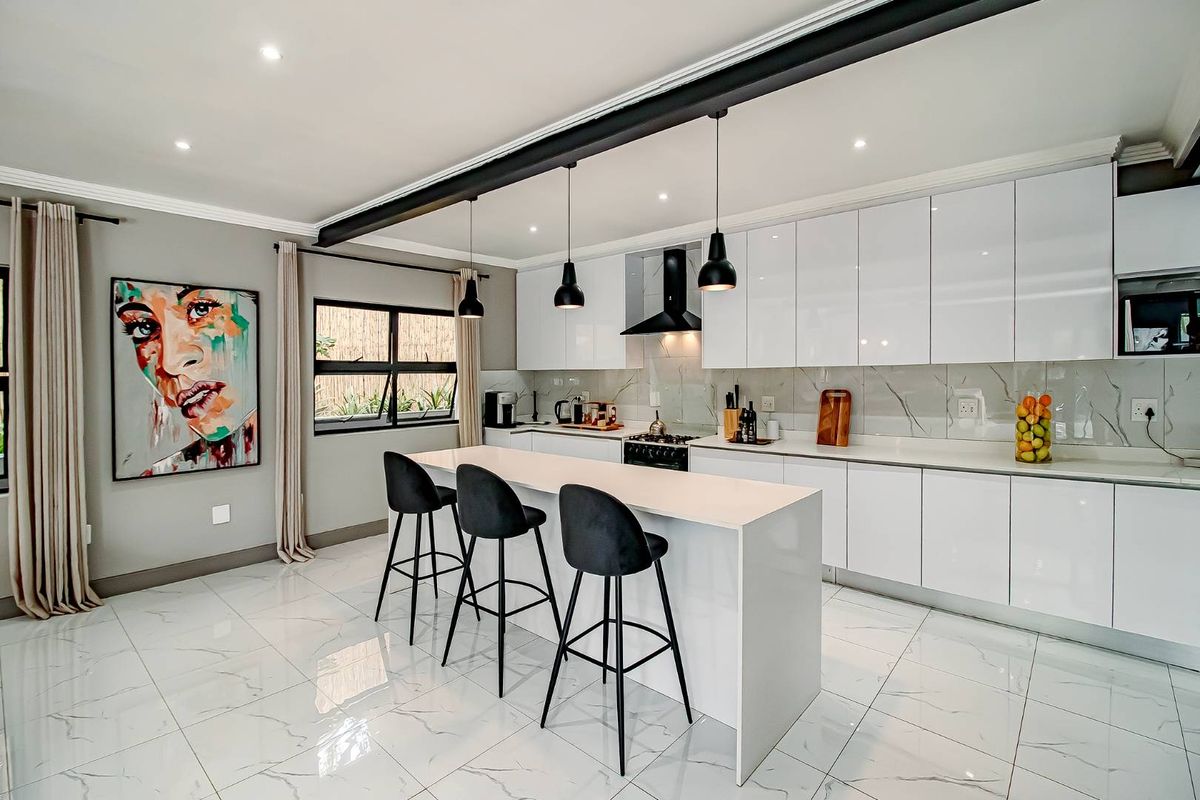 Modern, high-end kitchen featuring a central island, sleek white cabinetry, marble-look tiled flooring, and contemporary pendant lighting.
