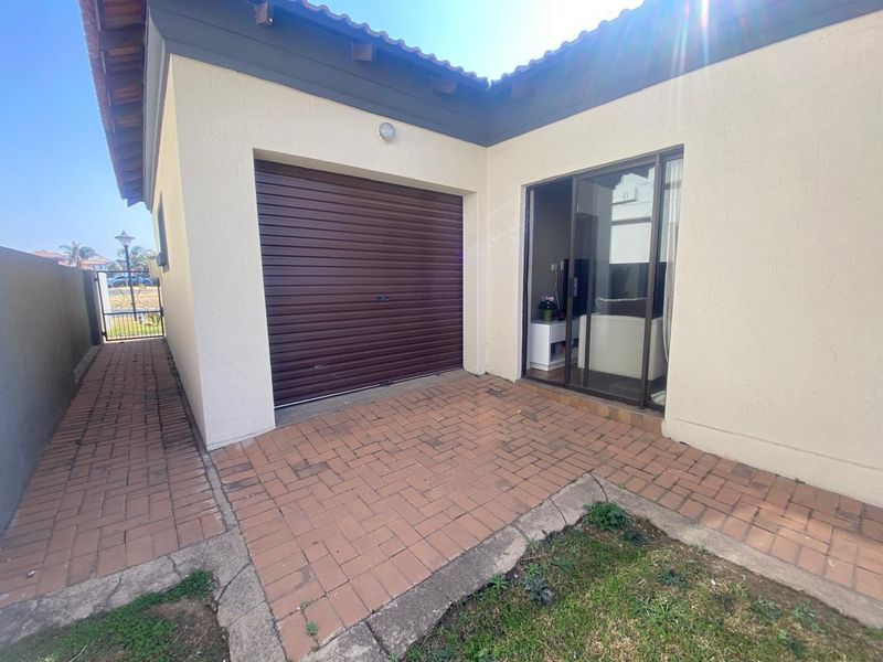 Rear exterior view featuring a brick-paved patio area, a roller garage door, and a sliding glass door providing access to the interior.