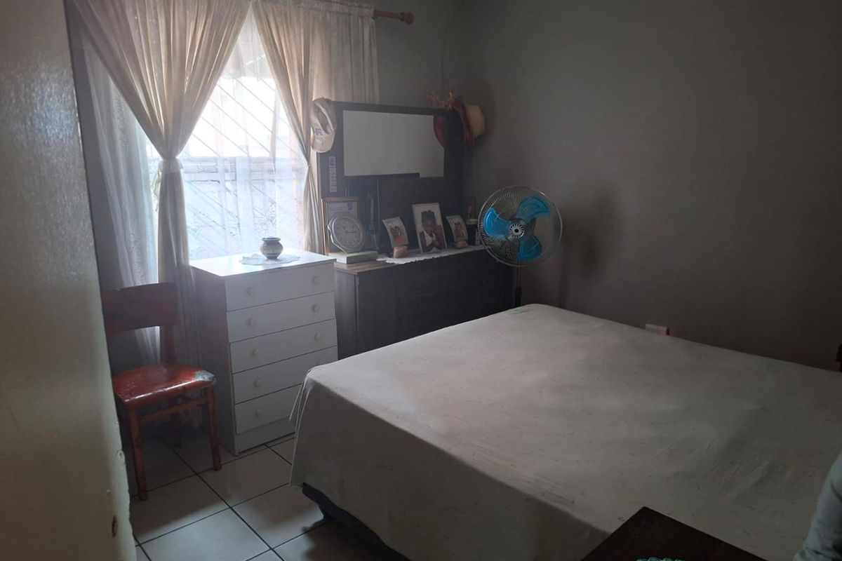 A standard bedroom featuring tiled flooring, a window with security bars, and neutral wall finishes.