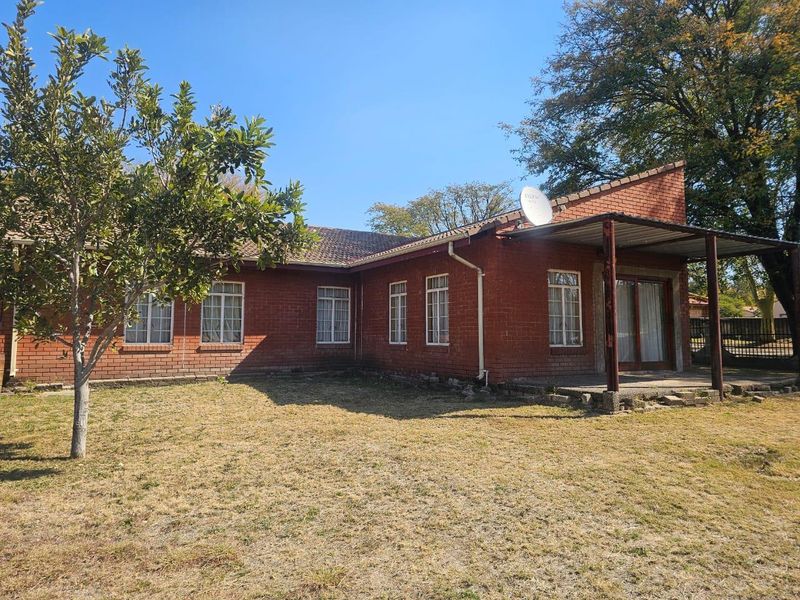 Rear view of a face brick house featuring a covered patio area, sliding glass doors, and a spacious garden.