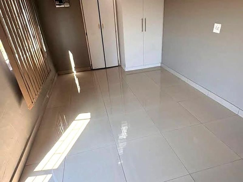 A clean, empty bedroom featuring neutral tiled flooring, built-in cupboards, and vertical blinds, offering a versatile space ready for personalization.