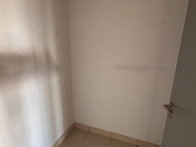 A small, empty office space featuring tiled flooring and a standard internal door, requiring minor cosmetic updates to the wall finishes.