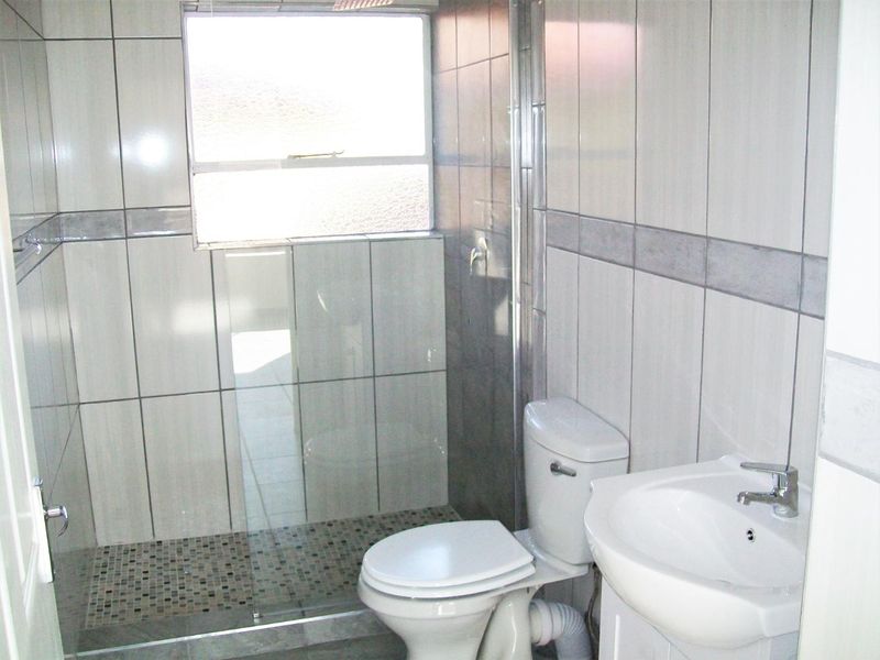 A clean, tiled bathroom featuring a walk-in shower with a glass screen, a pedestal basin, and a standard toilet.