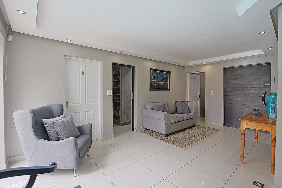 A bright living room featuring polished porcelain floor tiles, recessed downlighting, and multiple interior doors leading to adjacent rooms.