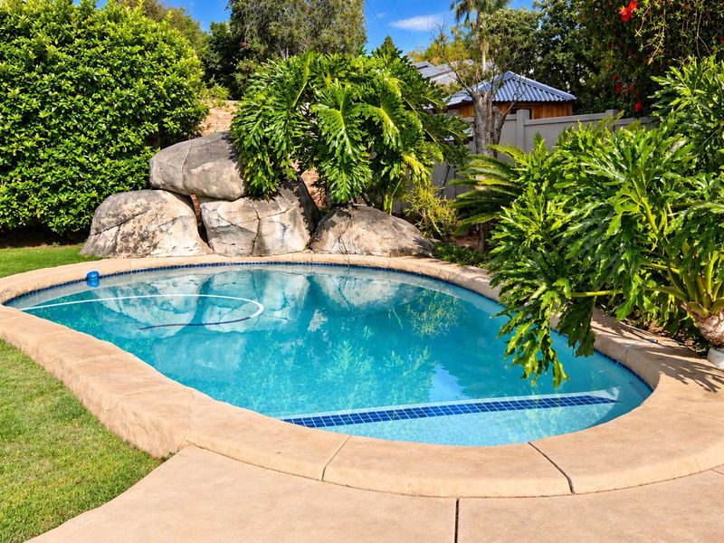 A well-maintained swimming pool area featuring natural rock landscaping, lush greenery, and paved surrounds, creating a private outdoor retreat.