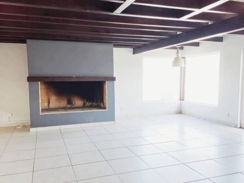 Spacious living area featuring exposed timber ceiling beams, tiled flooring, and a prominent built-in fireplace, offering a bright and open layout.