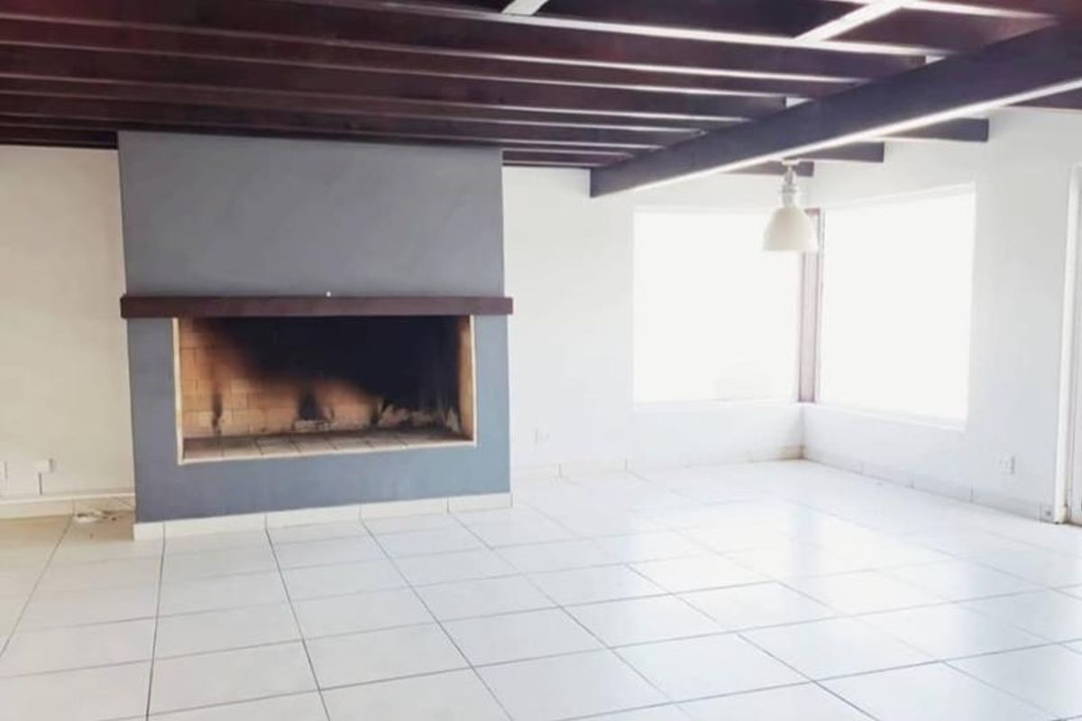 Spacious living area featuring exposed timber ceiling beams, tiled flooring, and a prominent built-in fireplace, offering a bright and open layout.