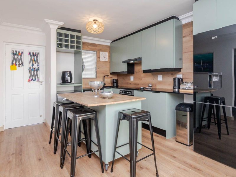 Modern kitchen featuring light green cabinetry, wood-look backsplash, a central island with seating, and integrated appliances.