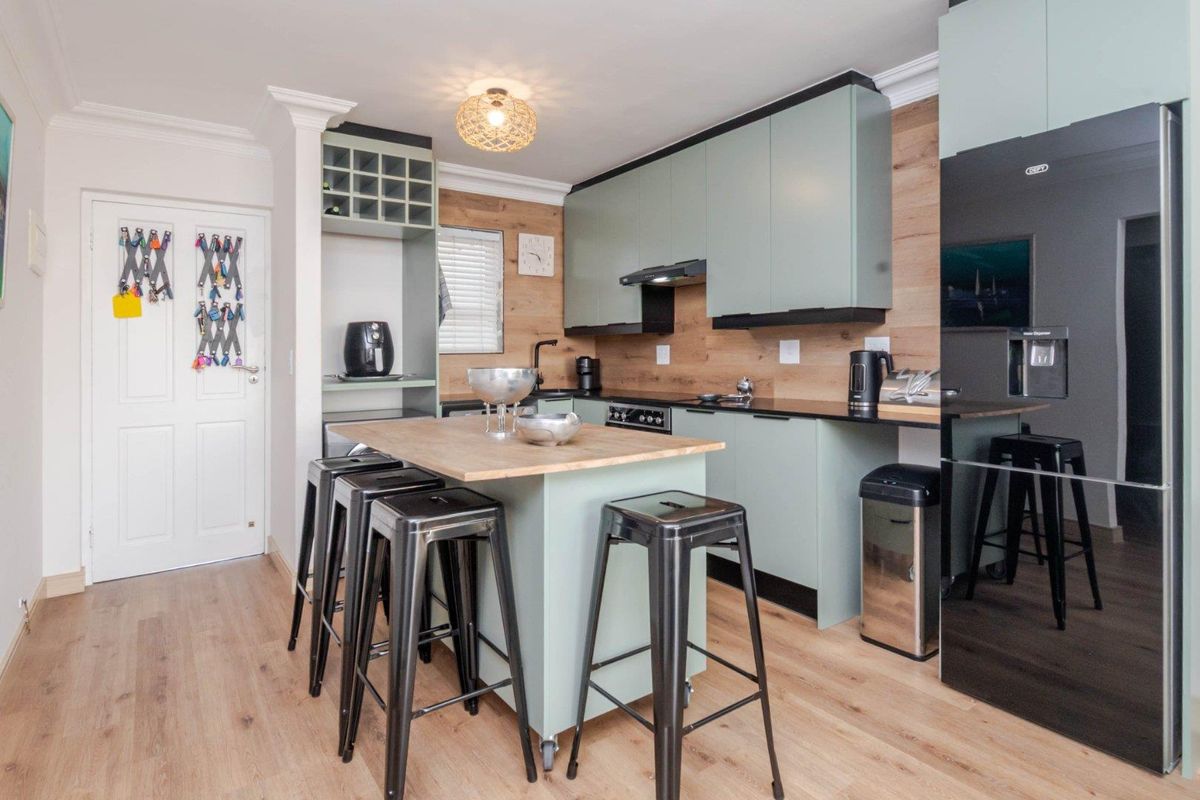 Modern kitchen featuring light green cabinetry, wood-look backsplash, a central island with seating, and integrated appliances.