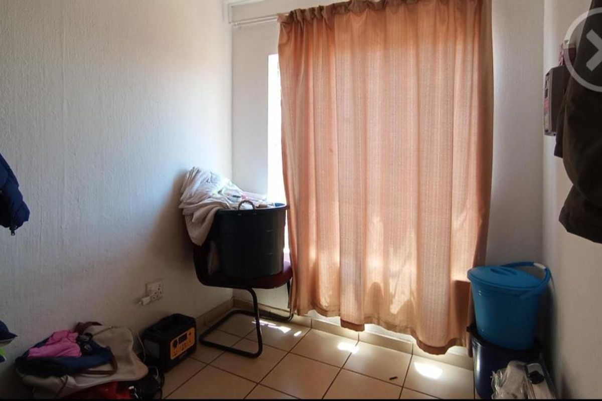 A small bedroom or utility space featuring tiled flooring and a window covered by curtains.
