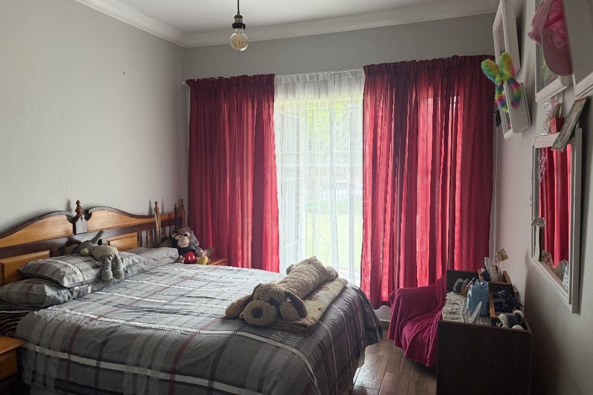 A comfortable bedroom featuring laminate flooring, neutral wall finishes, and large windows dressed with floor-to-ceiling curtains.