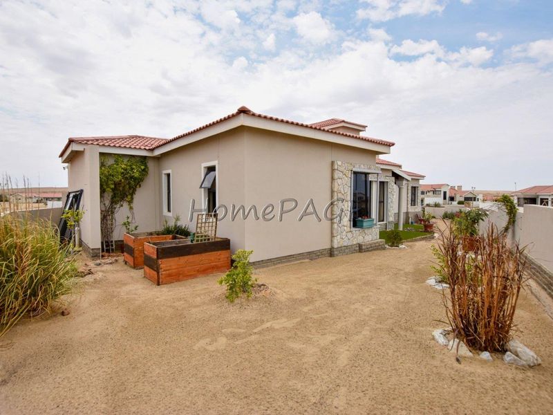 Rear view of a residential house featuring stone cladding accents, terracotta roof tiles, and a low-maintenance sandy garden area with boundary walls.