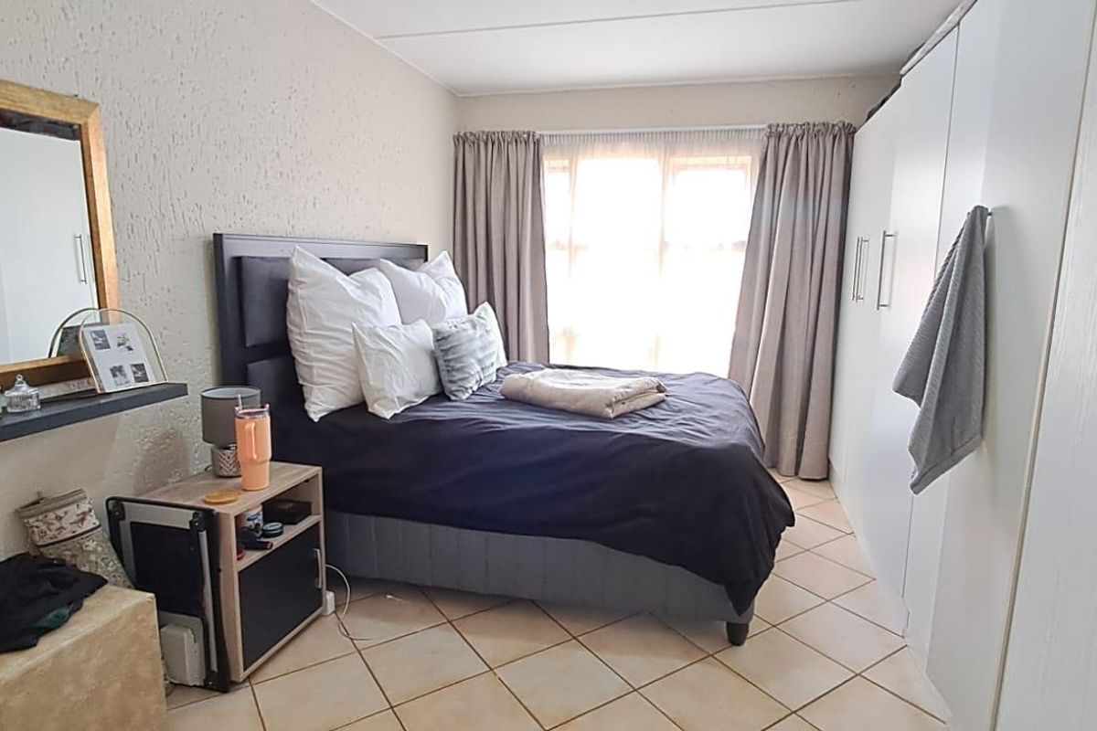 A bedroom featuring built-in wardrobes, tiled flooring, and natural light through a window with curtains.