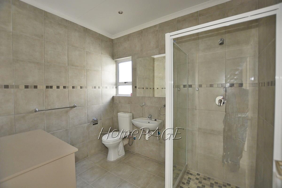 A modern bathroom featuring neutral wall and floor tiling, a glass-enclosed shower, a wall-mounted basin, and a toilet.