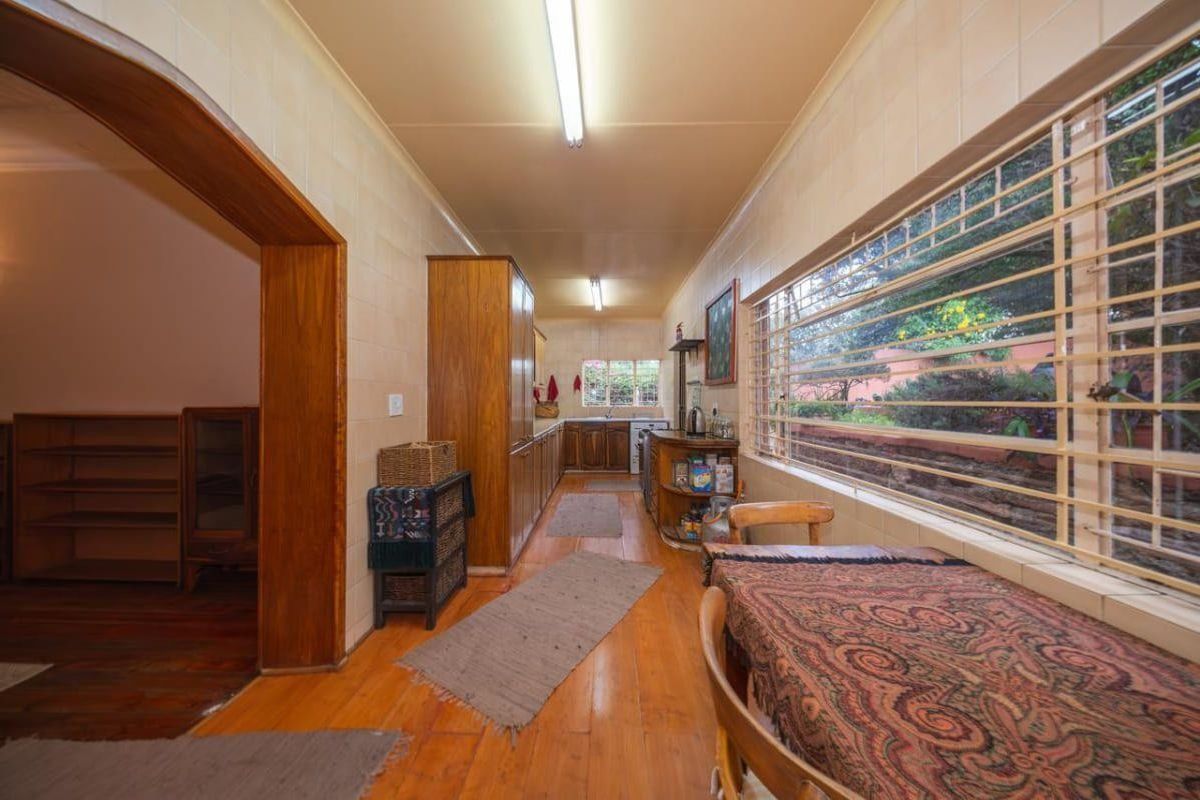 A long, galley-style kitchen featuring timber cabinetry, tiled walls, and large windows with security bars, providing a functional workspace with a view.