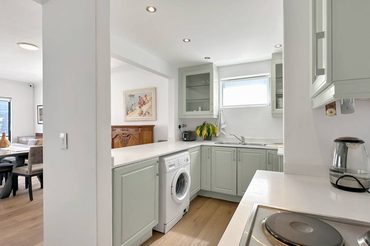 A bright, well-maintained kitchen featuring light green cabinetry, laminate countertops, integrated laundry facilities, and modern recessed lighting, seamlessly connected to the dining area.