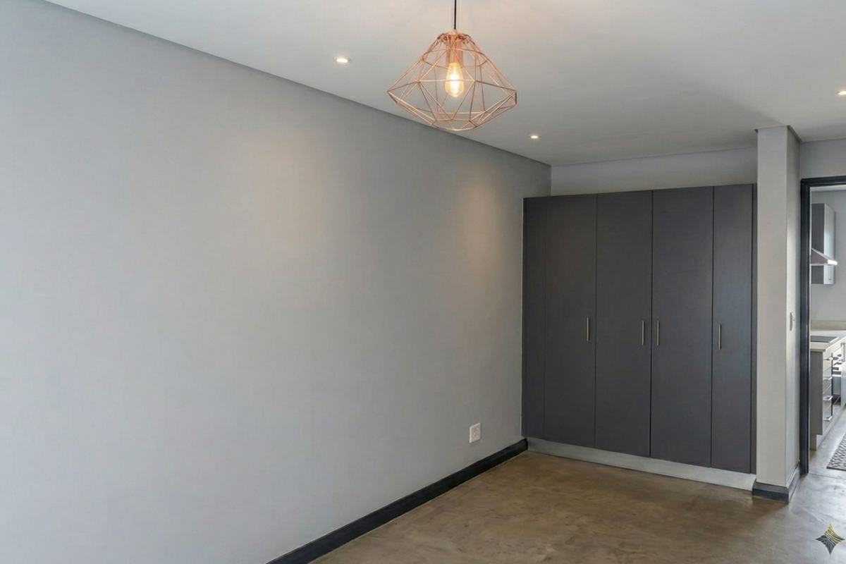 A modern, minimalist living area featuring polished concrete floors, neutral grey walls, and sleek built-in storage cupboards.