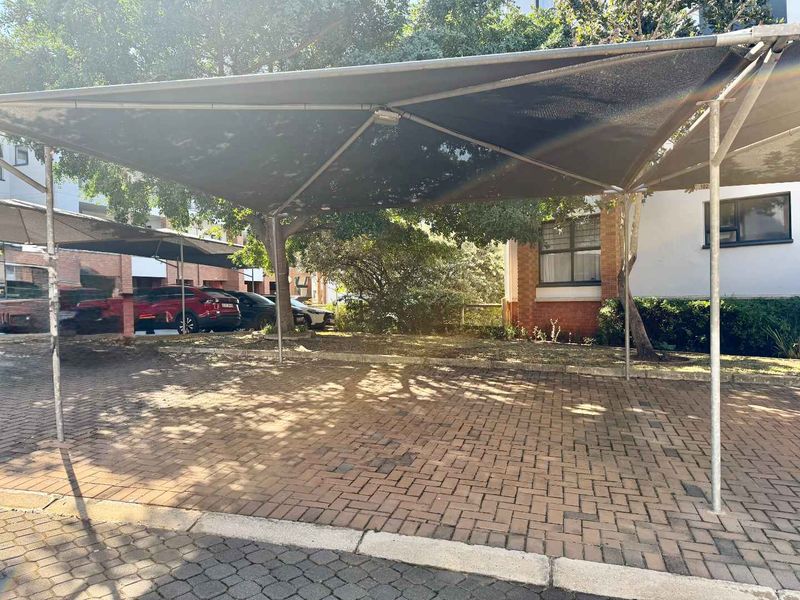 Covered carport parking area featuring a shade cloth structure and paved surface, located adjacent to the apartment building facade.