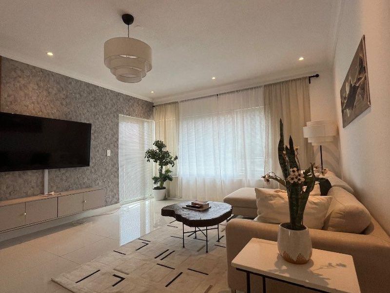Modern living room featuring polished tiled floors, a textured feature wall with integrated cabinetry, and ample natural light through large windows.