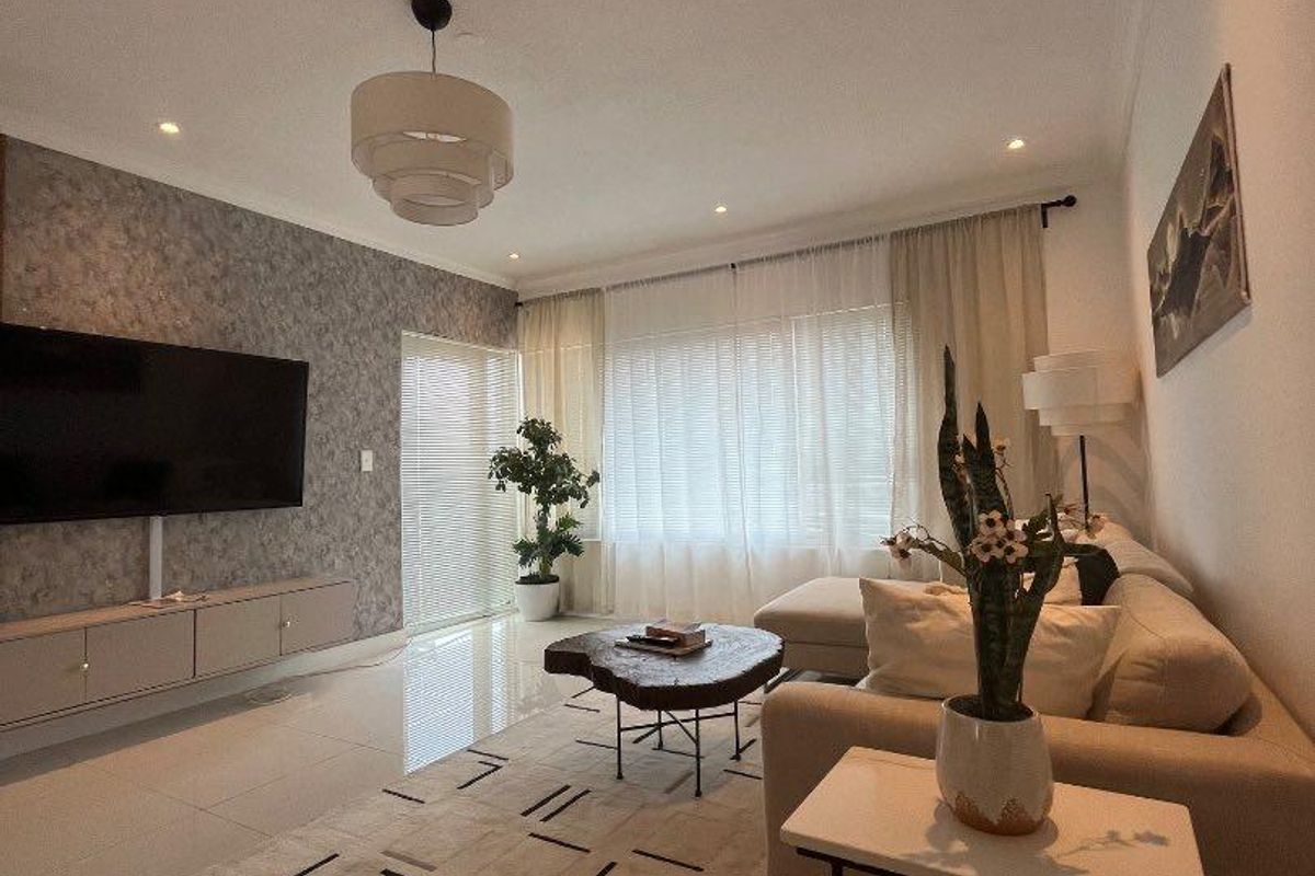 Modern living room featuring polished tiled floors, a textured feature wall with integrated cabinetry, and ample natural light through large windows.