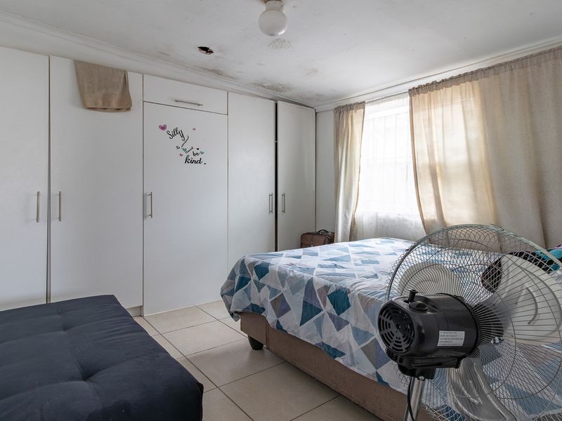 A bedroom featuring built-in cupboards and tiled flooring, currently showing signs of ceiling water damage and requiring maintenance.
