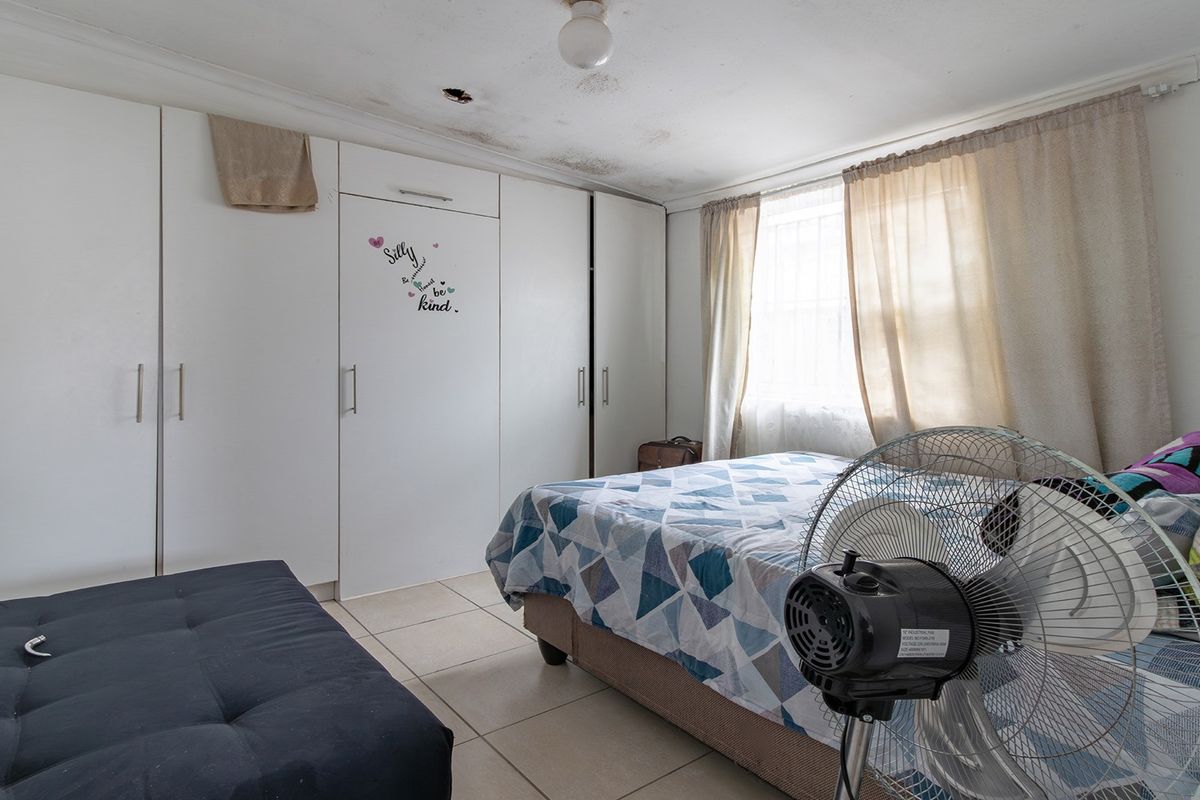 A bedroom featuring built-in cupboards and tiled flooring, currently showing signs of ceiling water damage and requiring maintenance.