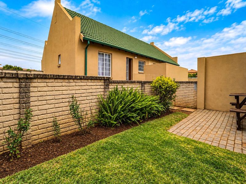 A well-maintained rear garden featuring a paved patio area, lawn, and a brick boundary wall, set against the townhouse exterior.