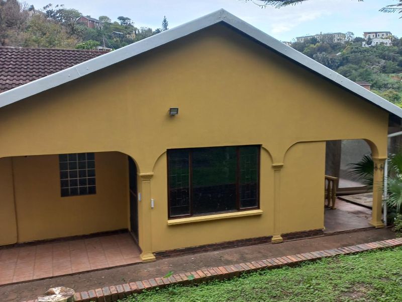 Rear view of the house featuring a covered patio area with arched columns, tiled flooring, and a combination of standard and glass block windows.