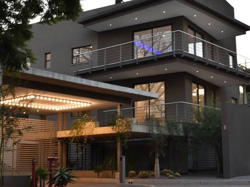Modern multi-story apartment building exterior featuring a covered driveway, balconies with stainless steel railings, and contemporary architectural lighting.