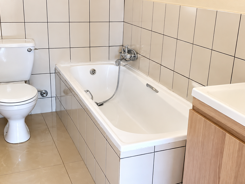 A clean, functional bathroom featuring a bathtub with handheld shower mixer, a white toilet, and a modern vanity cabinet with a washbasin.