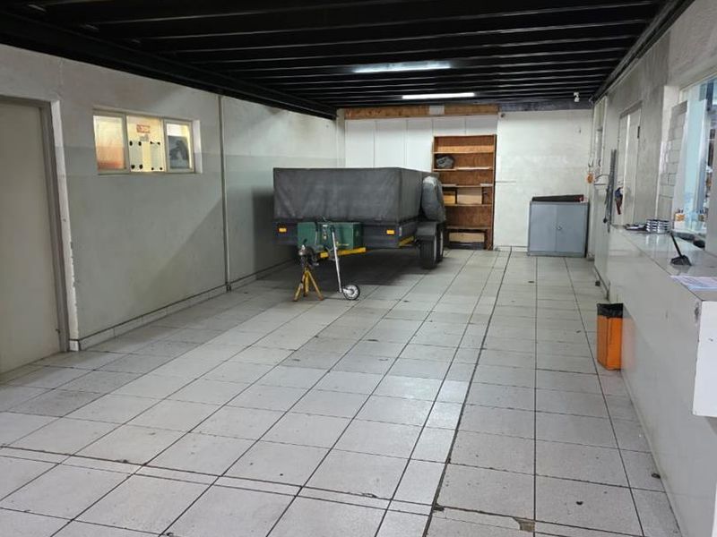 A functional workshop or utility space featuring tiled flooring, exposed steel ceiling beams, and built-in storage shelving and counter space.