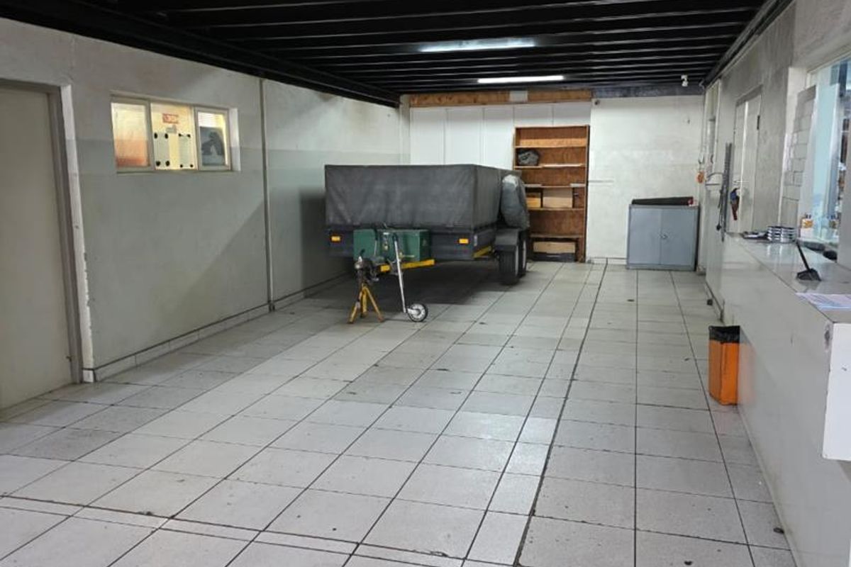 A functional workshop or utility space featuring tiled flooring, exposed steel ceiling beams, and built-in storage shelving and counter space.
