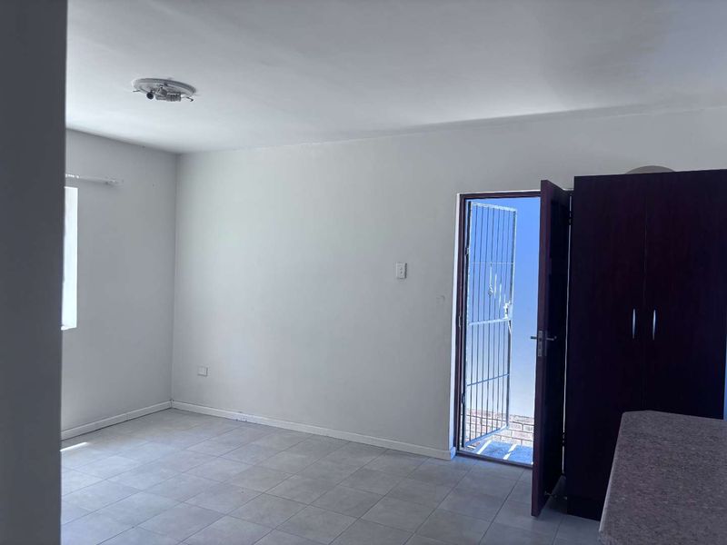An empty living area featuring tiled flooring, a security gate leading outdoors, and a built-in cupboard, offering a blank canvas for personalization.
