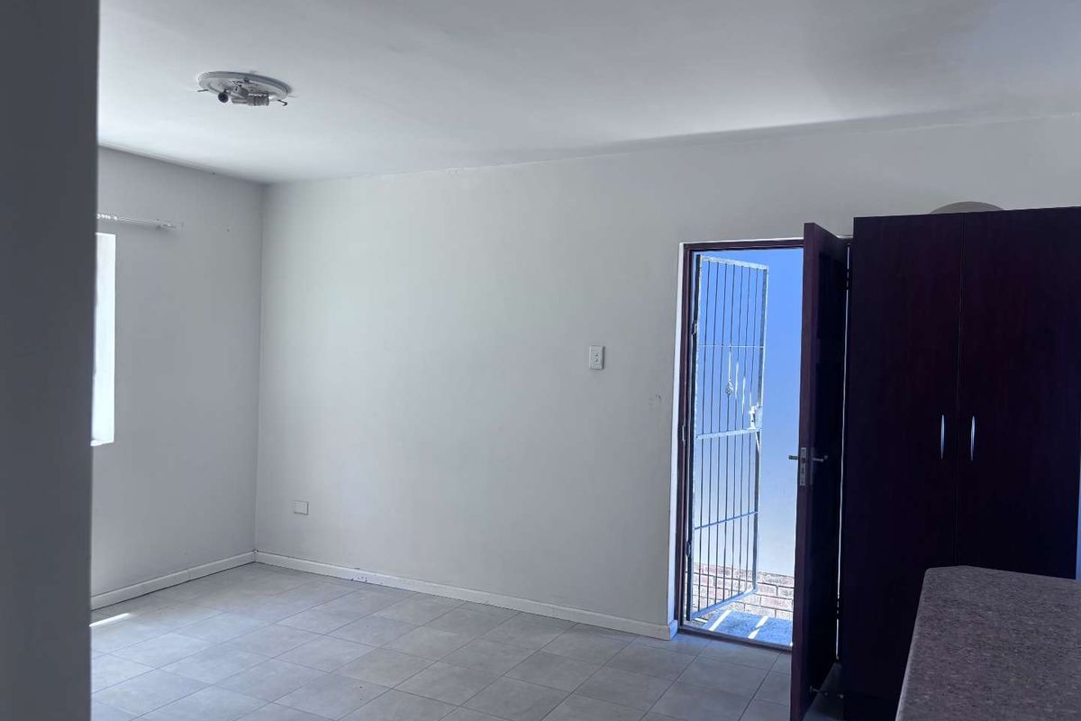 An empty living area featuring tiled flooring, a security gate leading outdoors, and a built-in cupboard, offering a blank canvas for personalization.