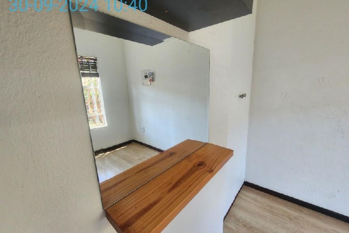 A vacant bedroom featuring laminate flooring, a built-in wooden shelf with a mirror, and a visible electrical distribution board.
